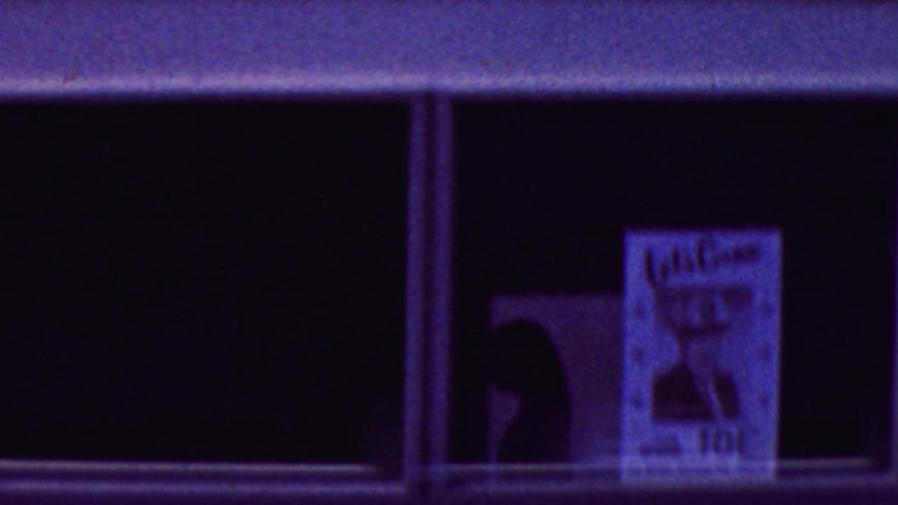 Purple-tinted 8mm frame of dark bus windows in California, with a poster in one window and a partial passenger silhouette nearby.