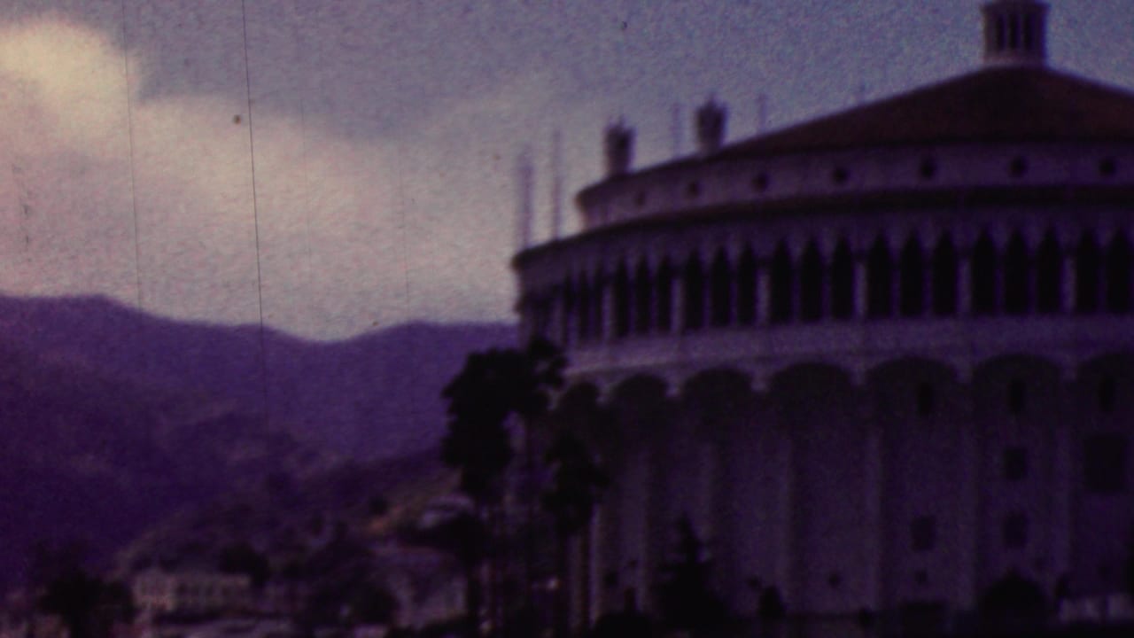 1961 California 8mm frame showing a large circular-looking waterfront building with arched windows, palm trees, and hills behind it.