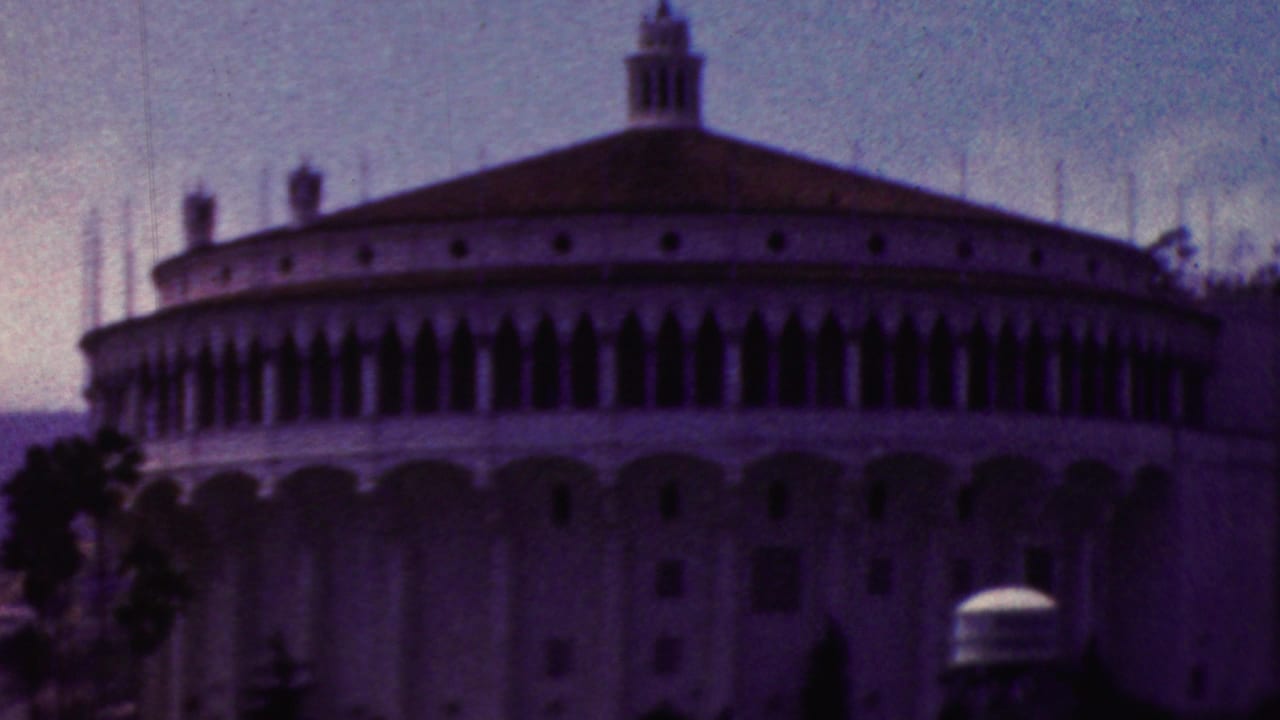 Visitor-shot 1961 California frame of the waterfront building, emphasizing its arched upper windows, broad roof, palm trees, and shaded facade.
