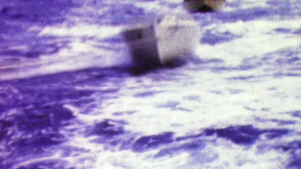 Soft, high-contrast 8mm frame showing bright rippling water and a small boat partly visible near the upper edge.