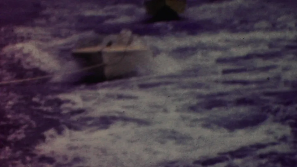 1961 California 8mm frame showing a small boat on the water near darker shoreline or dock forms, with visible grain and muted color shift.