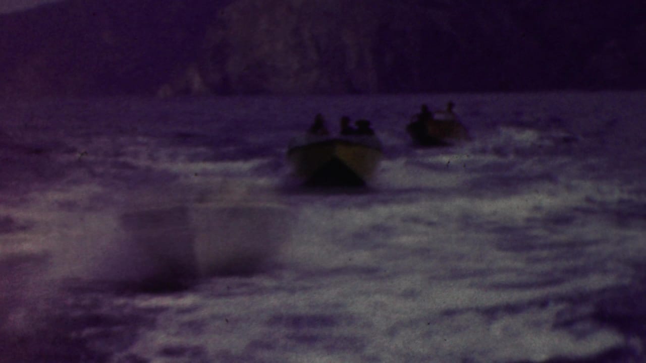 Small motorboats carrying distant passengers speed across choppy coastal water near rocky cliffs in California, based on the supplied clip metadata.