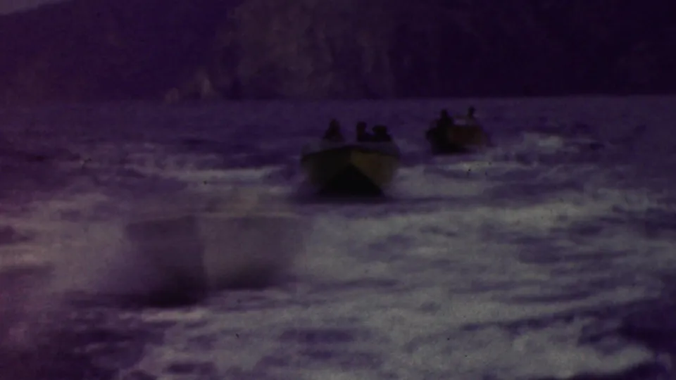 Small motorboats carrying distant passengers speed across choppy coastal water near rocky cliffs in California, based on the supplied clip metadata.