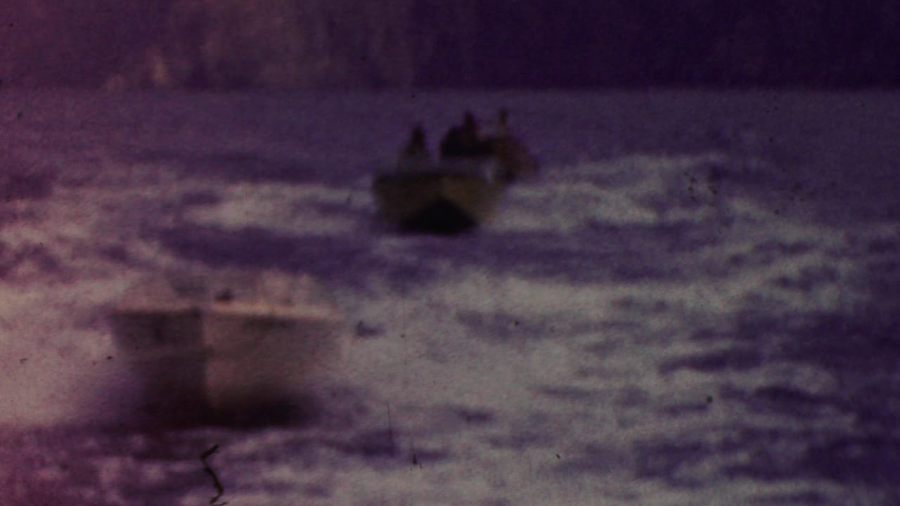 A blurred boat passes through foamy waves with other boats behind it.