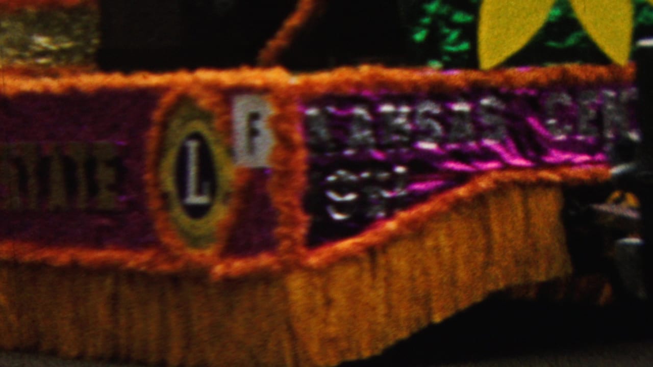 Decorated float side with purple tinsel, gold fringe, sunflower shapes, and a circular Lions emblem.