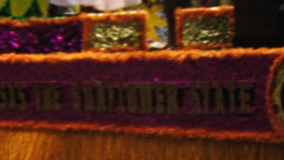 1961 California home-movie frame showing the lower side of a decorated parade float with lettering that appears to read The Sunflower State.