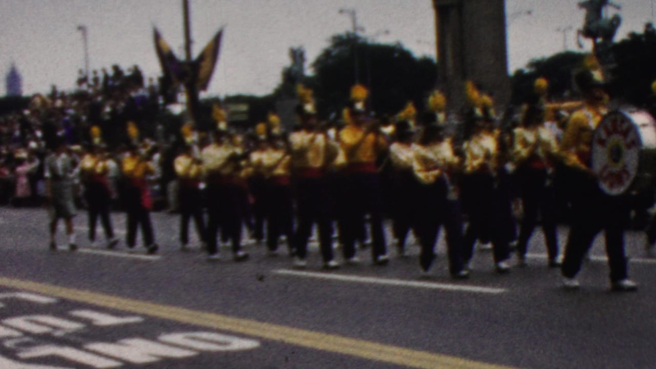 1961 California 8mm frame showing a Kentucky marching band in gold-and-black uniforms moving along a parade route before seated and standing spectators.