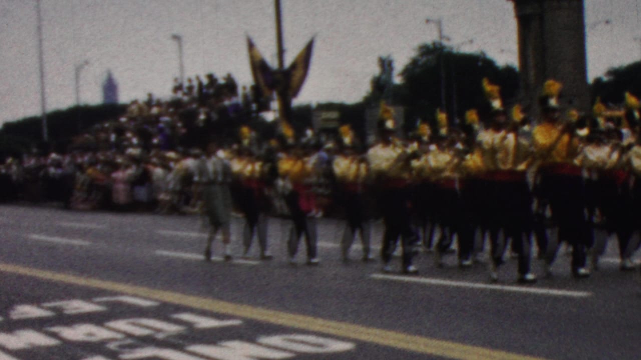 Band members march in formation with a bass drum near the center of the street.