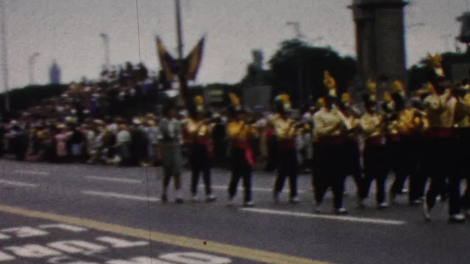 Curbside 8mm view of the Kentucky marching band continuing through a California street parade in 1961, with spectators gathered along the route.