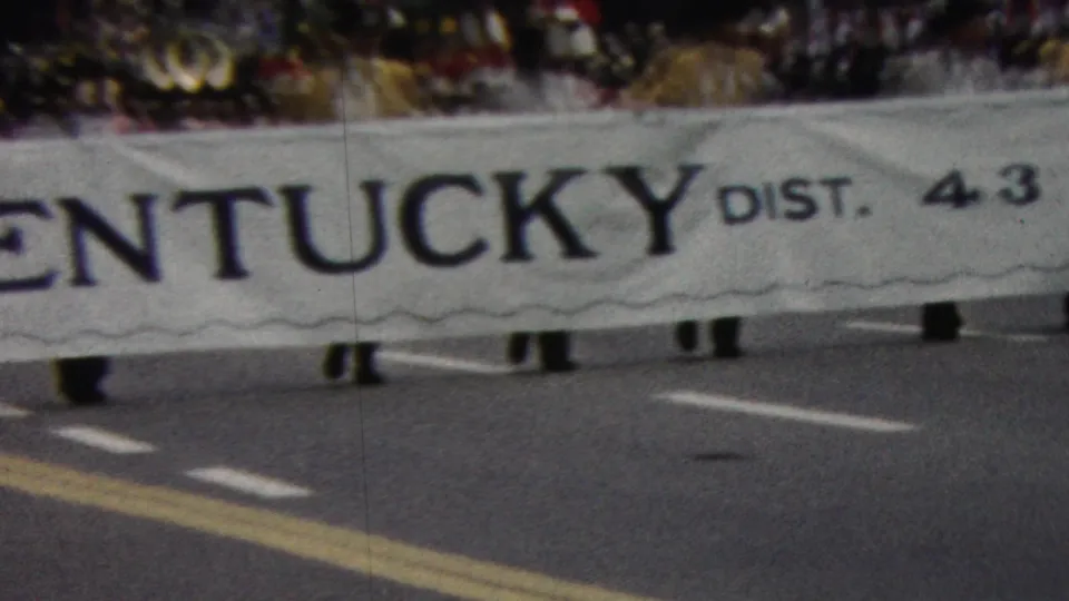 A low-angle 8mm view shows the Kentucky District 4.3 Lions banner moving along the parade route, with marchers mostly obscured by the cloth.