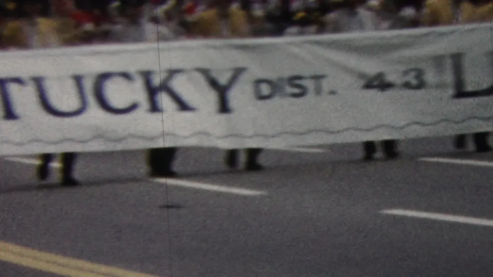 The closing frame shows the white Kentucky District 4.3 Lions banner filling most of the view, with marchers beneath it and spectators behind.