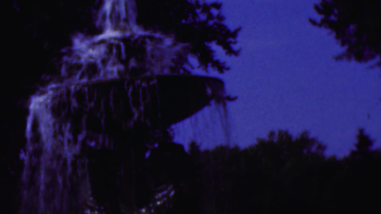 Tiered fountain seen closer, with water spilling over the upper bowl in purple-blue light.