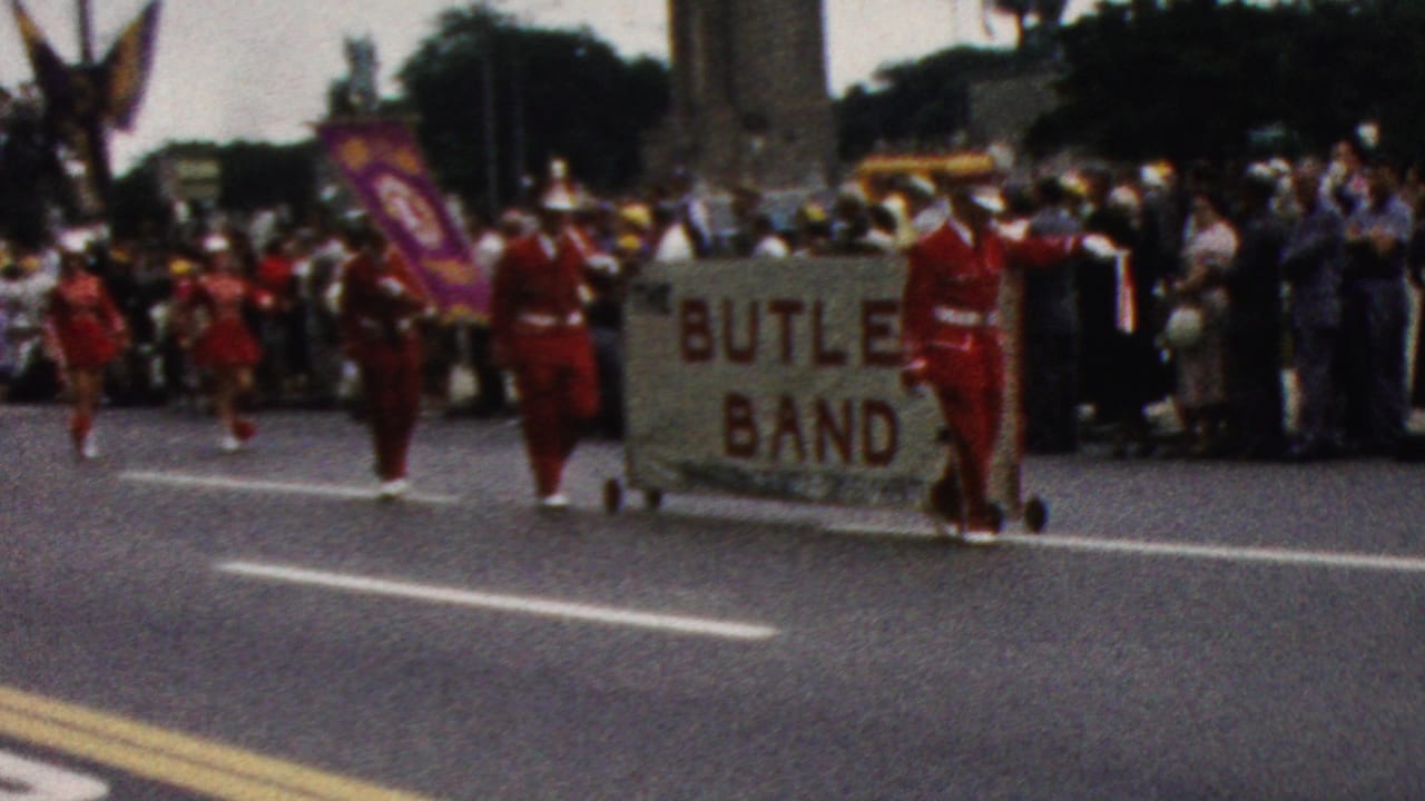 Marchers carry Butler Band banners past a crowd lining the street.