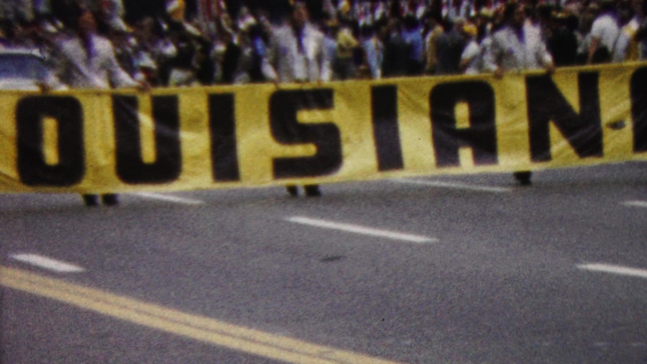 Yellow LOUISIANA banner fills the foreground with a crowd and car partly visible behind it.