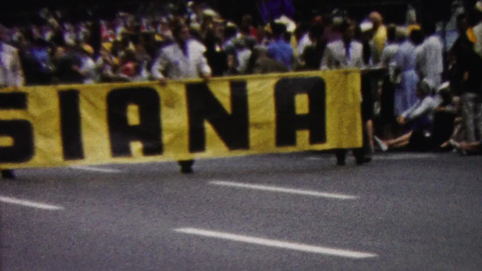 1961 California 8mm frame showing a close, cropped view of the LOUISIANA banner, several spectators in light clothing, and road markings in the foreground.