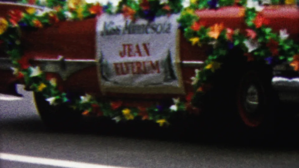 A red vehicle decorated with flowers carries a readable “Miss Minnesota” banner during the California parade, with spectators and street details around it.