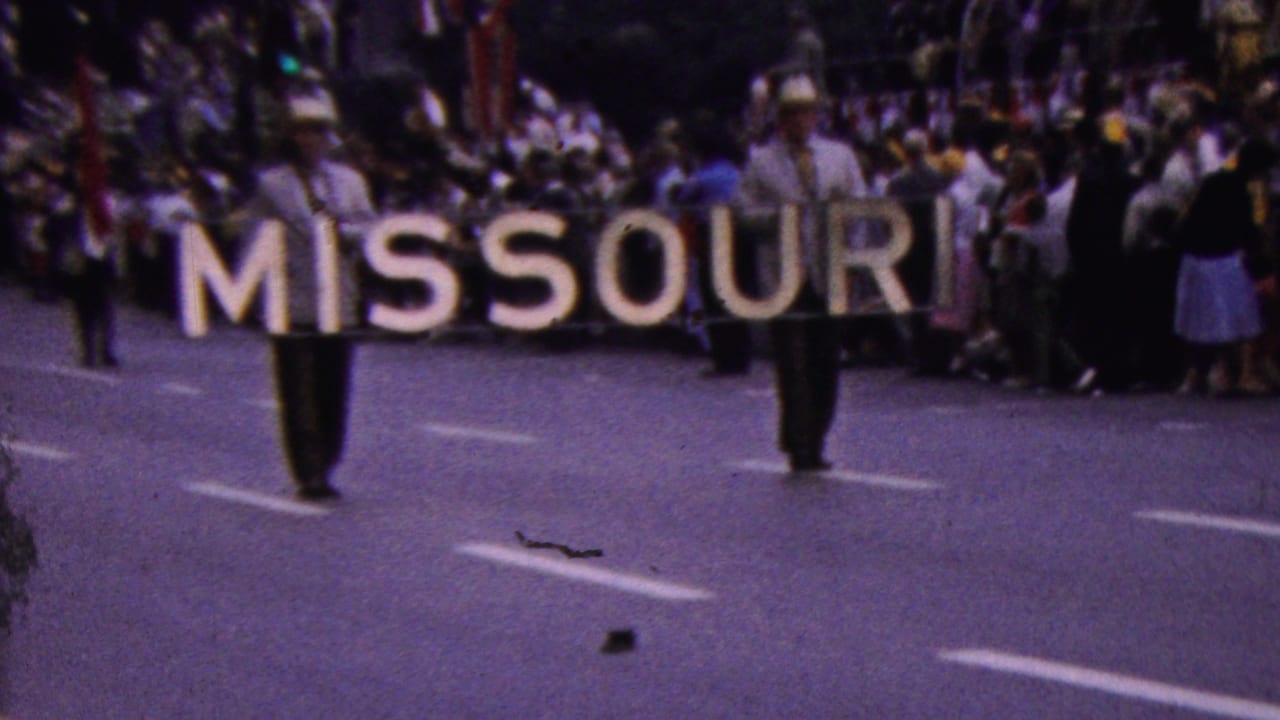 Two men carry a MISSOURI sign past spectators during a parade.