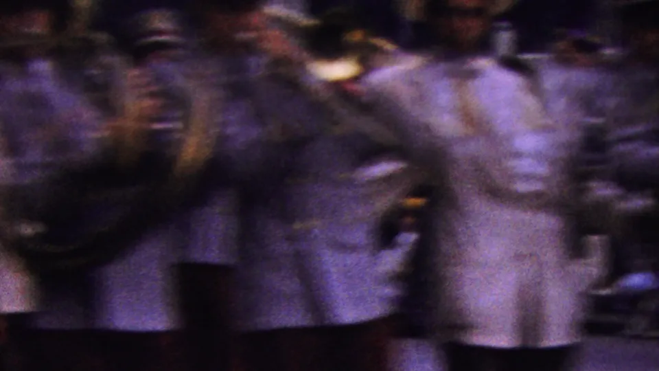 Motion-blurred band members in light jackets and red trousers pass very near the handheld camera during the 1961 California parade footage.