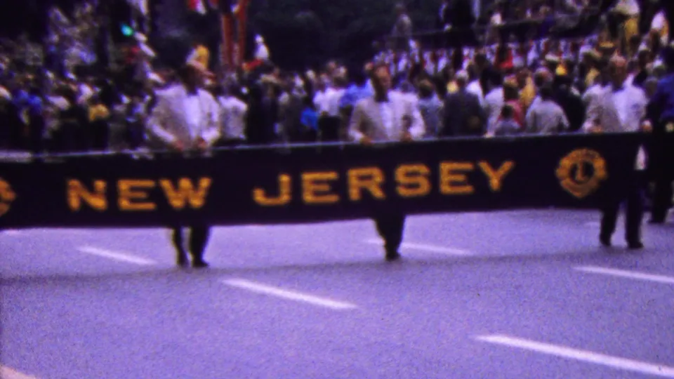 The NEW JERSEY banner moves along the 1961 California parade route, backed by a dense crowd, white-shirted participants, and visible Lions Club-style emblems on the banner.