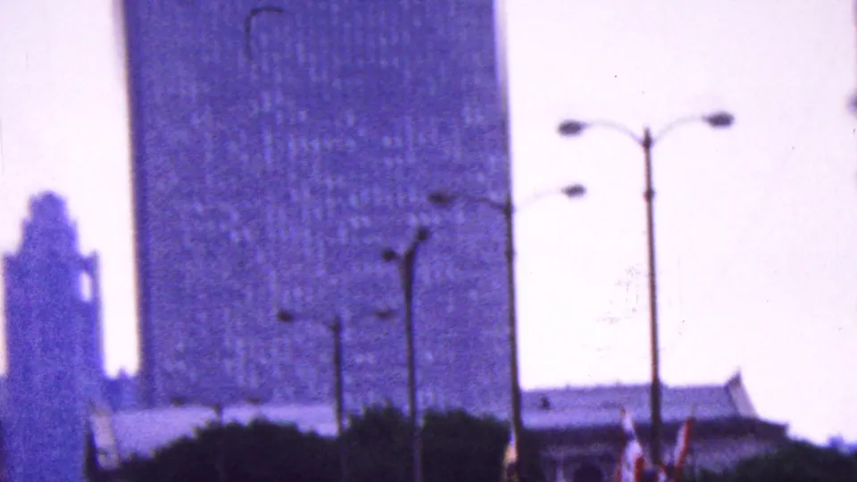 Purple-tinted 8mm view of a tall city building, lampposts, and bright sky, likely filmed as an urban cutaway during the same 1961 California home movie sequence.