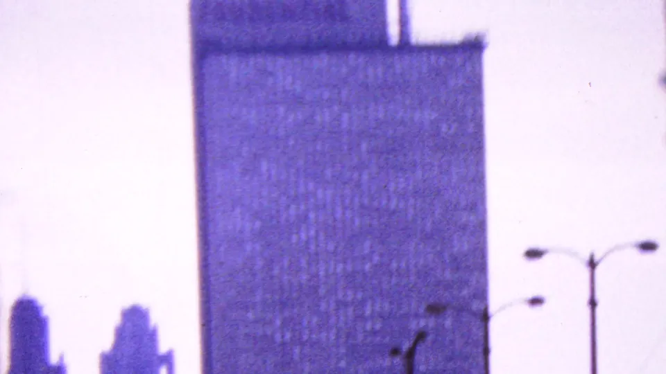 Handheld 8mm frame showing a tall rectangular high-rise with streetlights and a pale sky, presented as an urban architectural cutaway rather than an identified landmark.