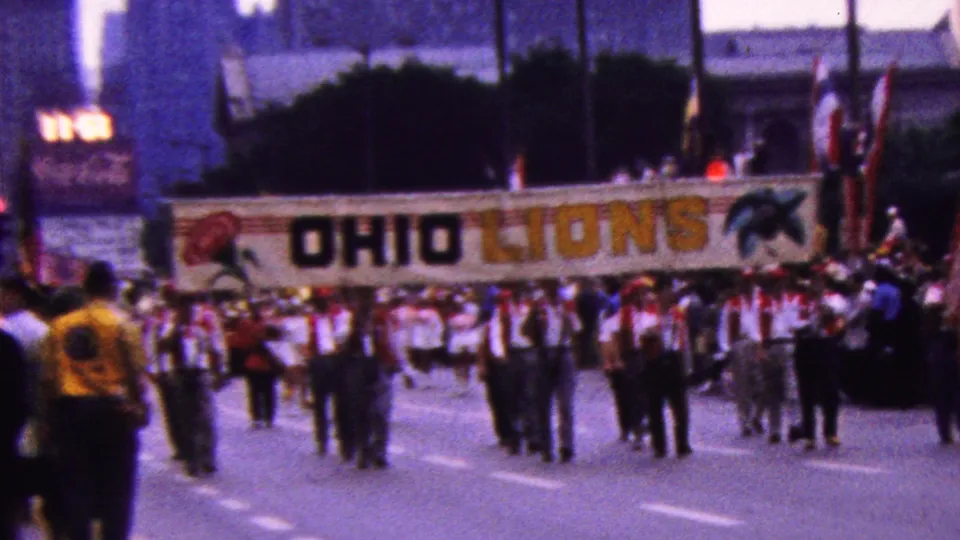 A marching group carries a large OHIO LIONS banner with emblem graphics along a California parade route, with buildings and flags visible in the background.