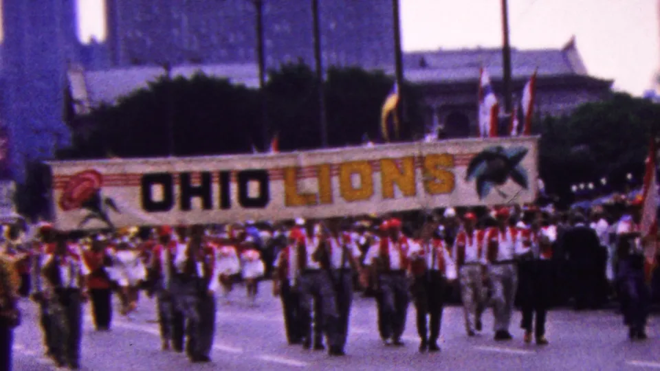 The OHIO LIONS banner fills the center of the frame as a uniformed marching group proceeds down the street in 1961 California home-movie footage.