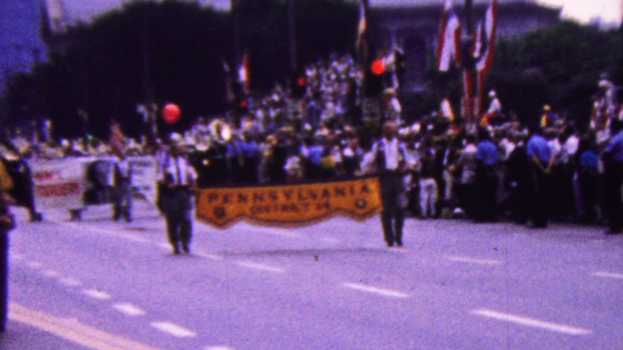 Parade group advances behind a yellow Pennsylvania District 14 banner with flags and musicians behind them.