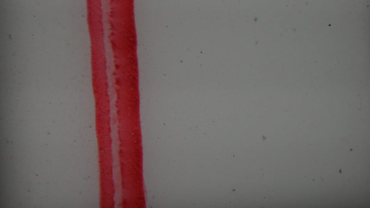 Red vertical streak on a pale surface with film dust and soft focus.