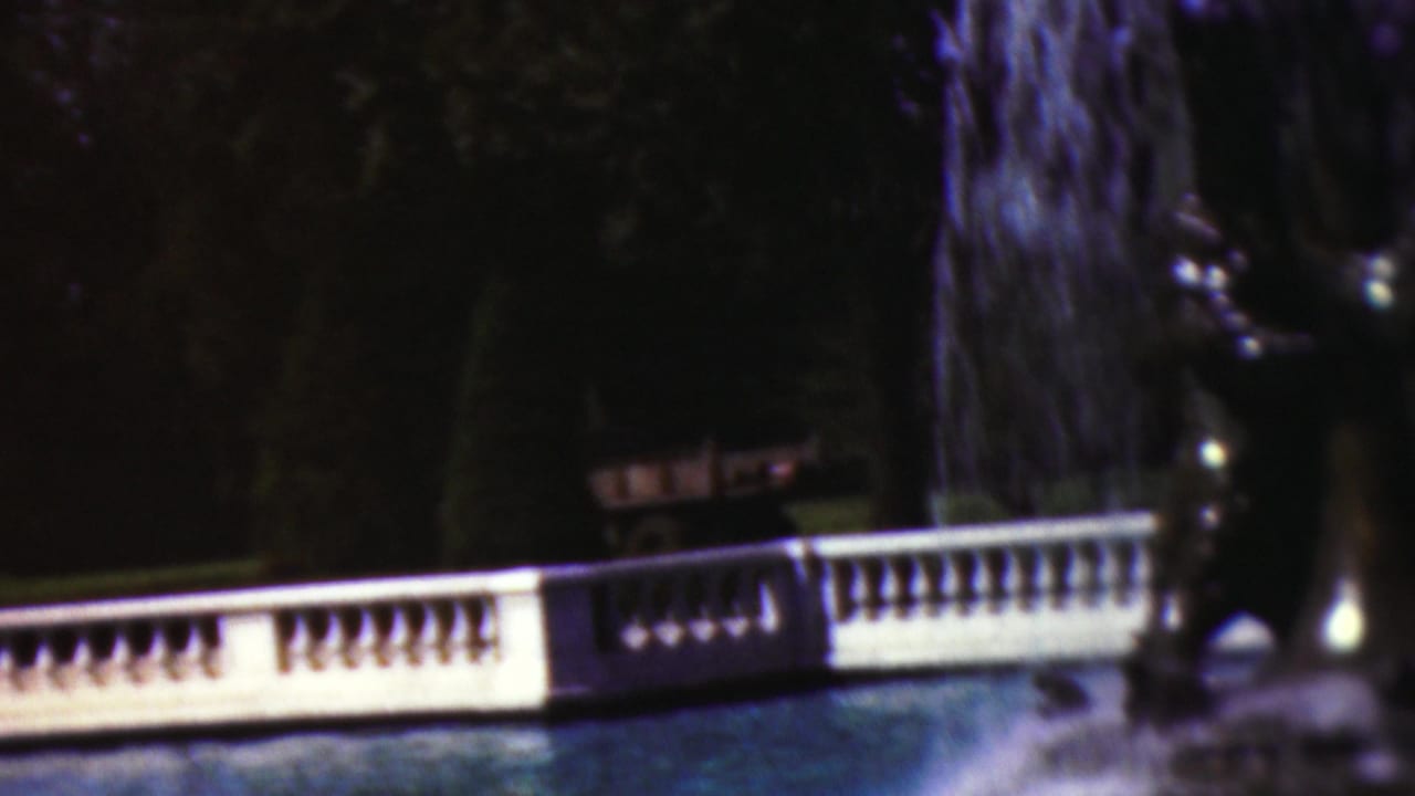 White balustrade and pool water with fountain spray against dark trees.