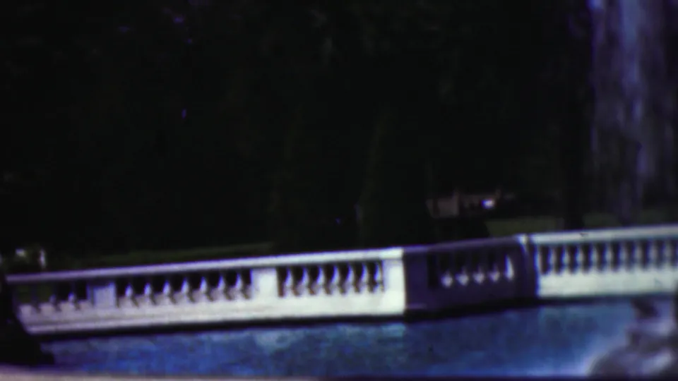 1953 Cleveland 8mm frame showing water spray above a white balustrade, a blue fountain pool, and a heavily shaded tree background.