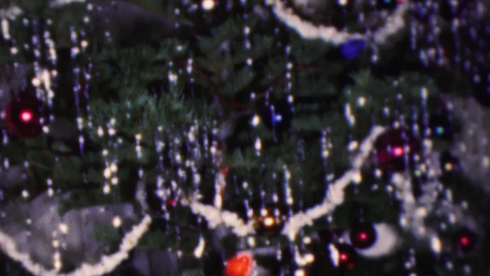 Final 1953 Cleveland frame showing a close tree detail with white garland, silver tinsel strands, small lights, and colored ornaments against dark evergreen branches.