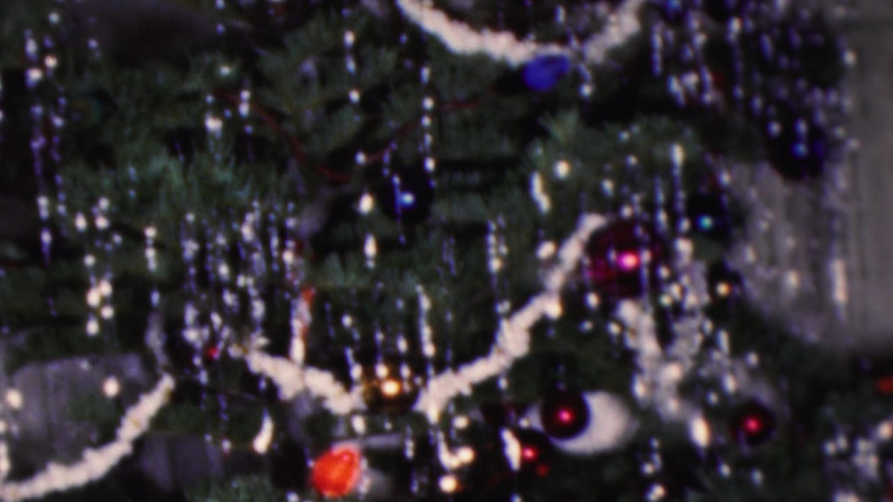 1953 Cleveland 8mm home-movie frame showing a close-up of a Christmas tree with silver tinsel, white garland, dark branches, red and blue ornaments, and a striped candy-cane decoration.