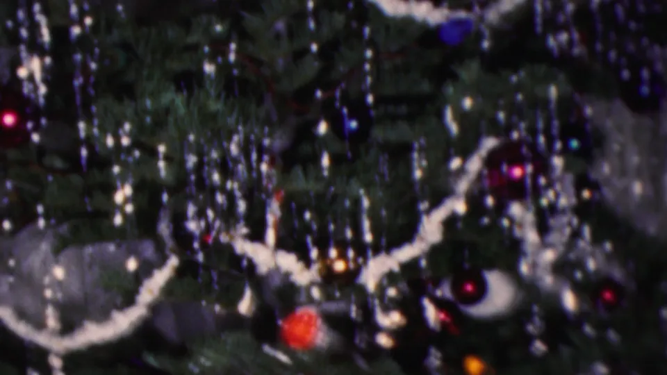 1953 Cleveland home-movie frame with white garland draped across a dark green Christmas tree, surrounded by silver tinsel, red and blue baubles, and small glowing lights.