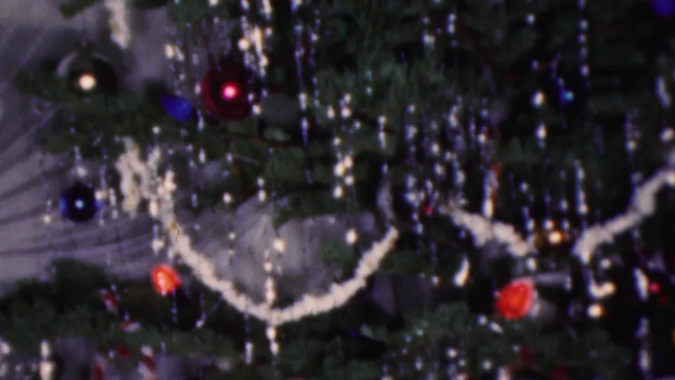 1953 Cleveland 8mm frame showing a crowded Christmas tree detail with dangling silver tinsel, white garland, blue baubles, red ornaments, and striped candy-cane decoration near the lower edge.