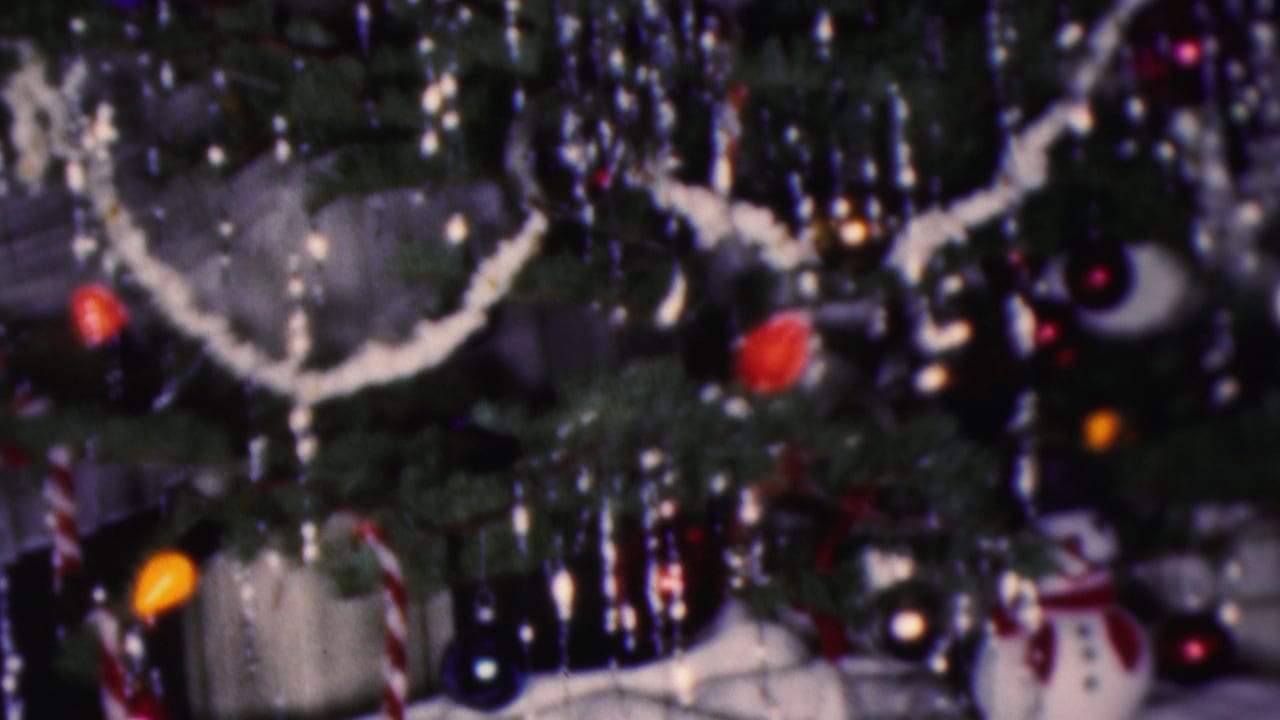 Decorated Christmas tree with white garland, ornaments, and small holiday figures below.