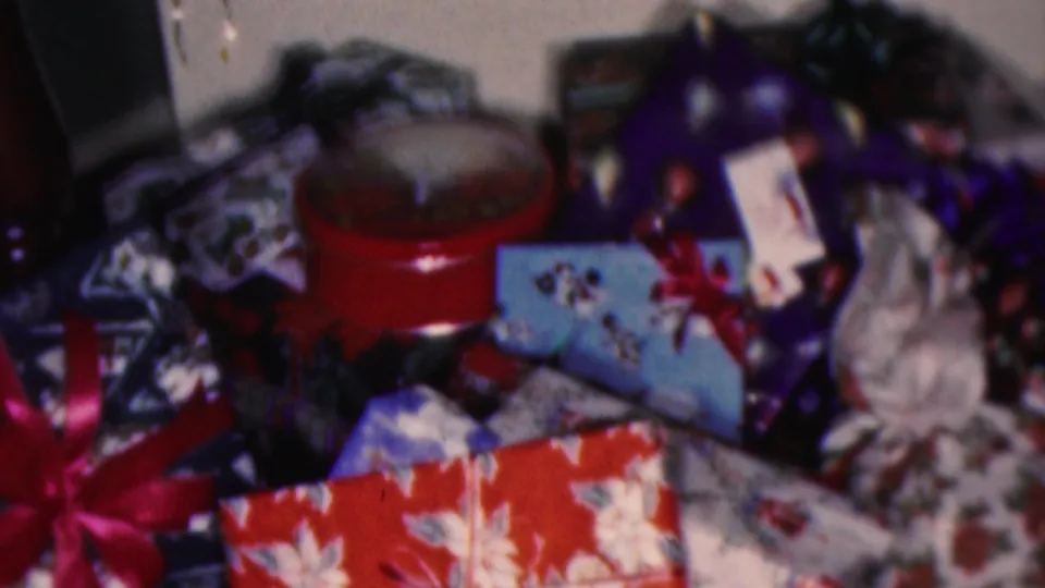 1953 Cleveland home-movie frame showing wrapped Christmas presents, ribbons, a red round box, and tree decorations in a domestic holiday setting.