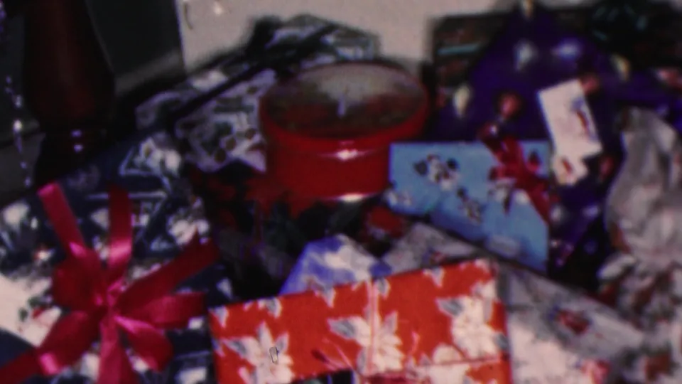 1953 Cleveland 8mm frame showing a pile of Christmas gifts with red floral wrapping, ribbons, a red round box, and ornaments under the tree.
