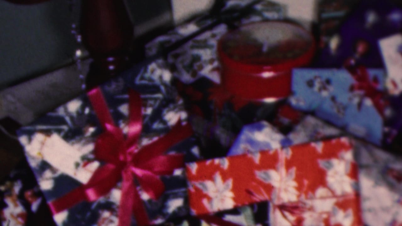 1953 Cleveland home-movie frame showing wrapped Christmas gifts with patterned paper, red ribbon bows, upholstered furniture, and a red round container nearby.