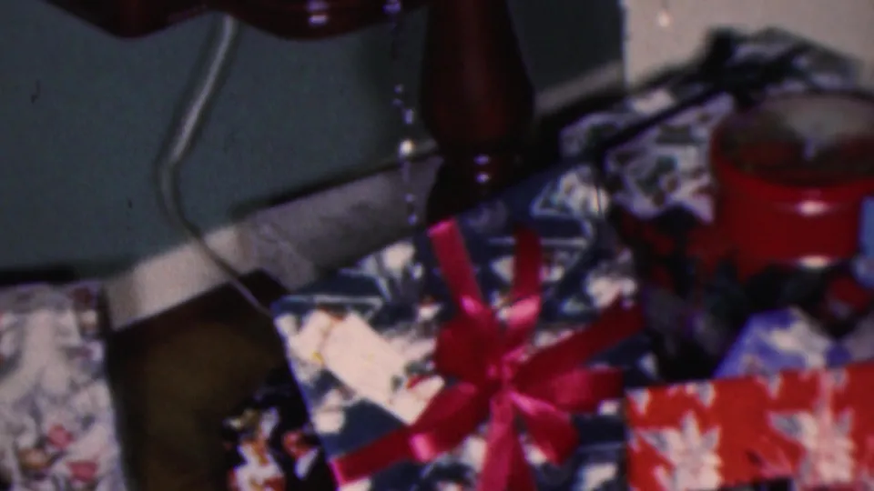 1953 Cleveland 8mm frame with a close view of colorful wrapped Christmas presents, a red bow, illustrated gift paper, and nearby furniture details.