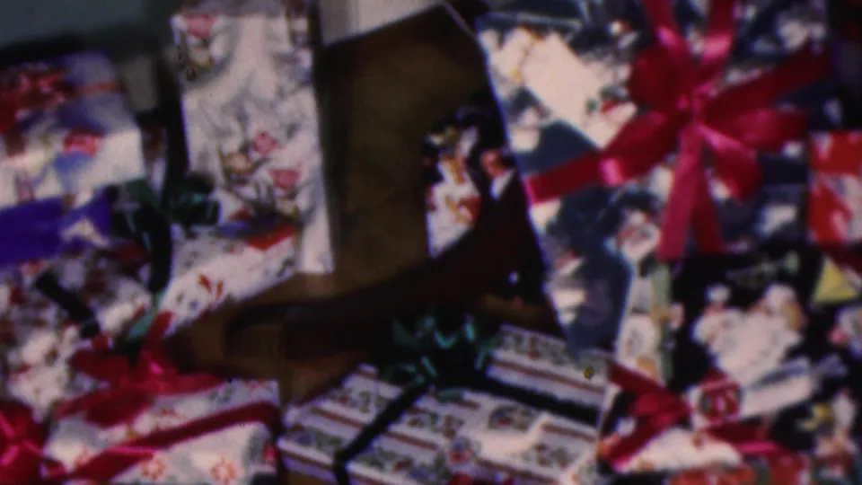 1953 Cleveland 8mm frame showing wrapped Christmas gifts with red and green ribbon bows, patterned paper, and dark wooden furniture in the background.