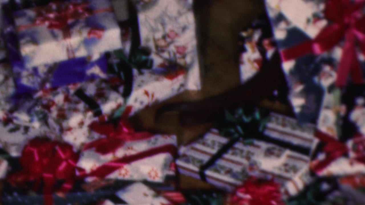 Cleveland, Ohio 1953 home-movie frame showing wrapped Christmas gifts with red and green ribbons on a wooden floor.