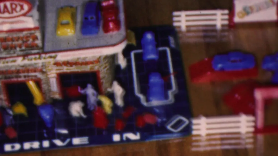 Cleveland, Ohio 1953 home-movie frame with a close view of the toy drive-in garage, miniature cars, figures, white fence sections, and floor play area.