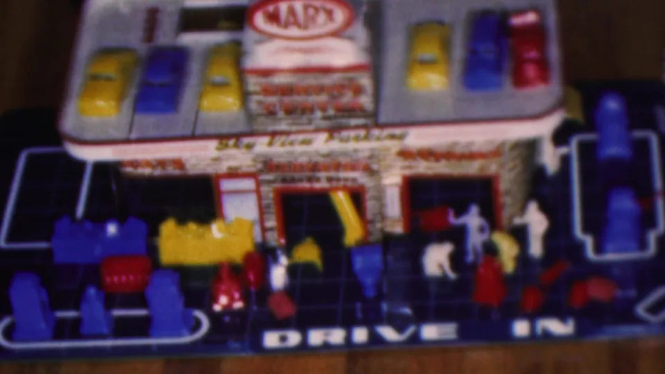 Cleveland, Ohio 1953 frame showing the toy garage playset from another angle, with cars on the roof area, drive-in lettering, figures, and colorful plastic pieces.