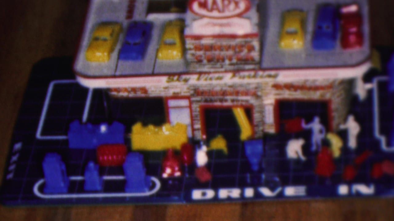 1953 Cleveland home-movie frame showing a Marx-style toy service center playset with roof parking cars, small plastic figures, garage bays, and Drive In lettering.