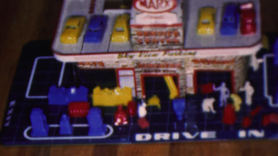 1953 Cleveland home-movie frame showing a Marx-style toy service center playset with roof parking cars, small plastic figures, garage bays, and Drive In lettering.
