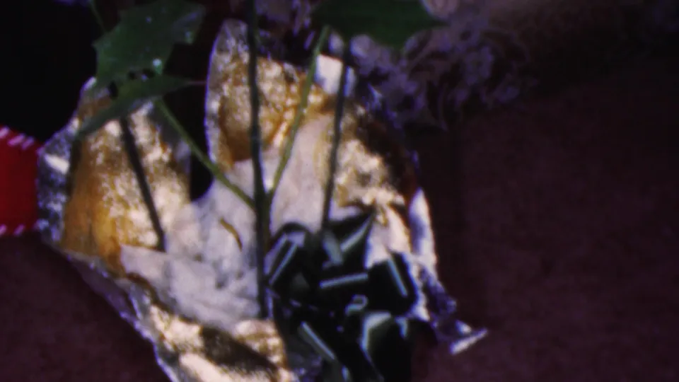 A gold wrapped holiday package with a dark striped bow appears in close-up beside poinsettia leaves in the 1953 Cleveland home interior.