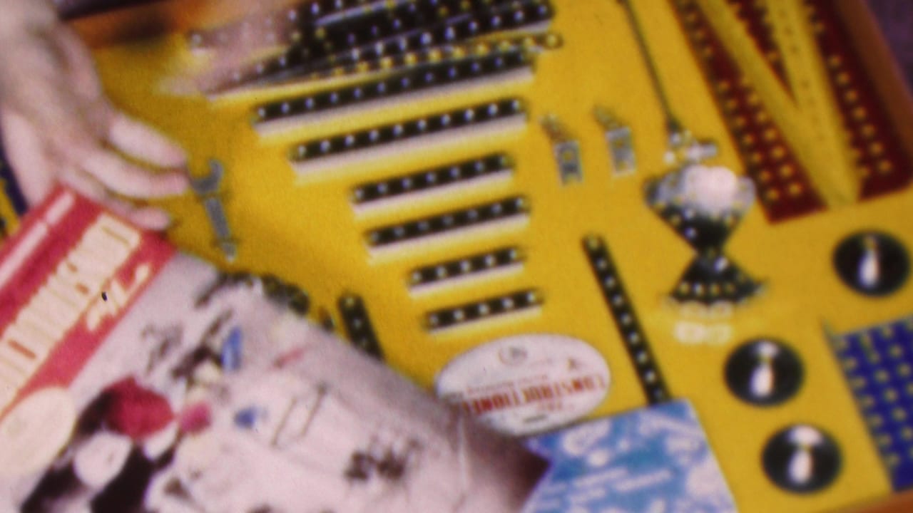 Hands near a yellow construction board with small tools and a printed instruction booklet.