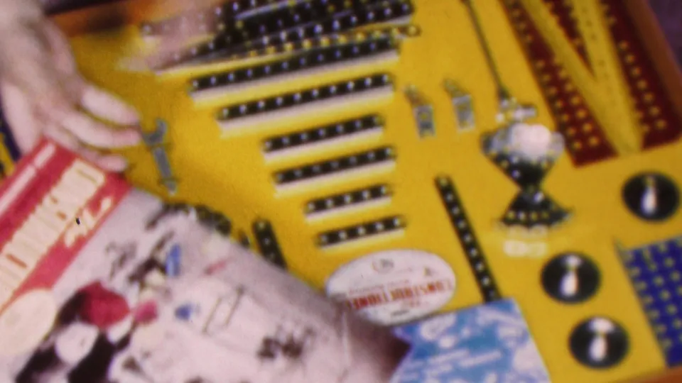 Close 1953 Cleveland home-movie view of hands working beside a yellow and blue construction set board, small wrenches, metal pieces, and a printed instruction booklet.