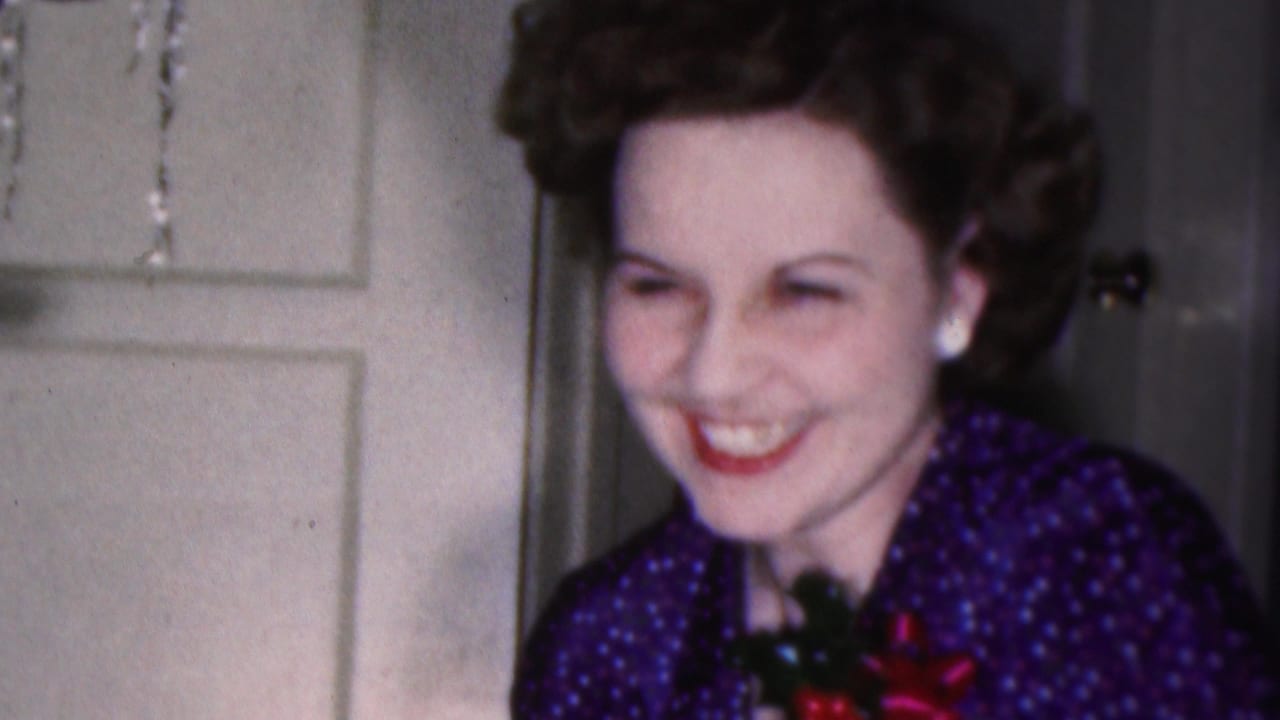 Woman smiling downward in festive attire by an interior door.